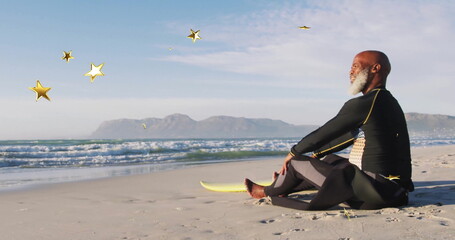 Sitting surfer in wetsuit gazing at sea on beach with yellow surfboard, star graphics, copy space
