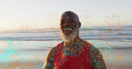 Standing senior man wearing red shirt smiling at beach at sunset, glowing teal and orange particles