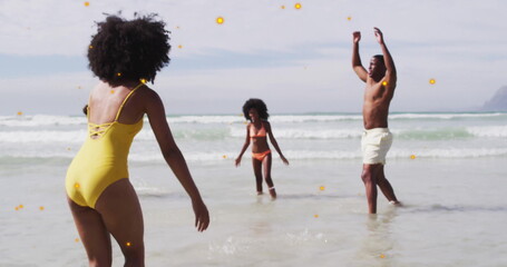 Playing family members tossing and catching in ocean water at beach, with swimsuits and swim trunks