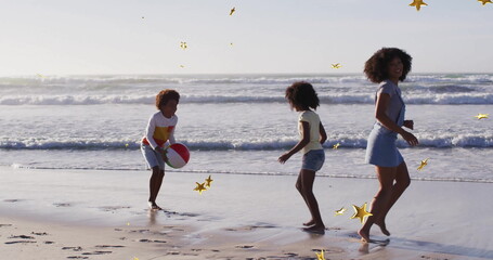 Playing mother and two children tossing beach ball on wet sand by ocean, with golden confetti