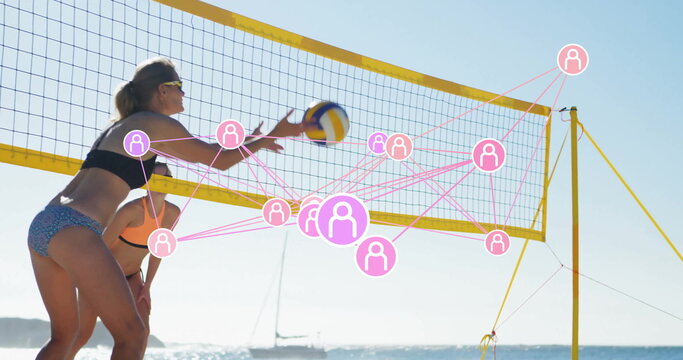 Spiking volleyball athlete in sports bikini jumping at shoreline net, with network icons