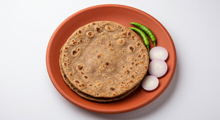 traditional Indian Gujarati food roasted flat bread ragi roti or finger millet bhakri with onion slice and chili pepper, on earthen clay tawa pan, white background, top view 