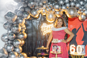 Woman celebrating 60th birthday posing at party with balloons and decorations