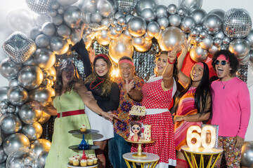 Friends celebrating 60s themed birthday party with silver balloons and disco balls