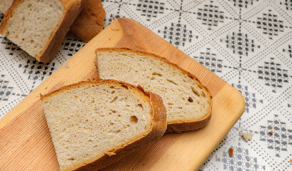 Sliced rustic bread on wooden cutting board. Freshly sliced bread placed over a patterned tablecloth. Perfect for breakfast or snacks. Selective focus.