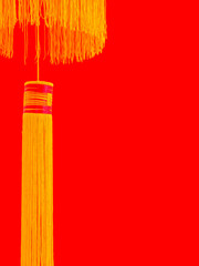 A section of a lantern with yellow gold threads and strings hangin against a red wall