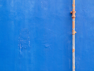 Blue wall with a peeled off seasoned painted round steel pipe.