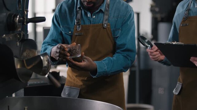 Multiethnic coffee factory workers Caucasian African American two men inspect roast beans magnifier glass quality aroma flavor checklist clipboard espresso control grind process machine manufacturing