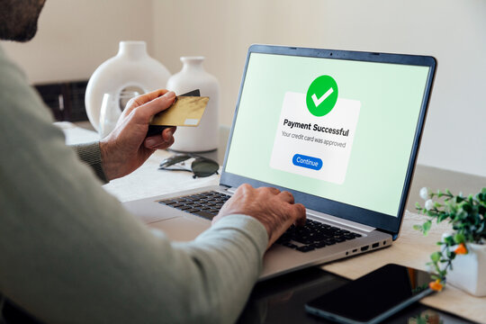 Making a credit or debit card payment online. Successful digital payment confirmation on a laptop screen. Man in his living room completing a purchase.