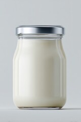 Clear glass jar filled with creamy white yogurt or dessert with silver metal lid isolated on a plain light background with soft lighting