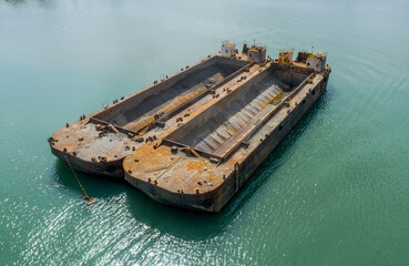 Two rusty sand barges floating on calm turquoise water, captured from above near an industrial port