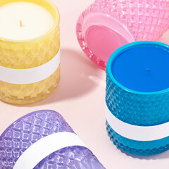 Colorful glass jar candles with blank labels on pastel background. Trendy scented candles in textured containers. Concept of home fragrance, self-care and customizable packaging. Close up