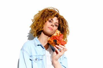 Young woman with curly hair enjoying a slice of pepperoni pizza against a white background,...