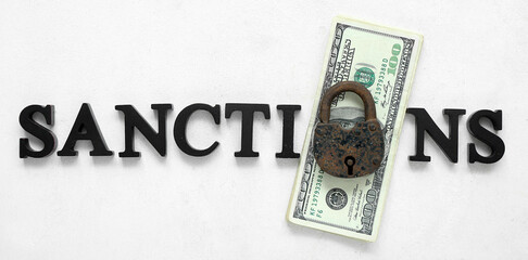 Word SANCTIONS with lock and dollar banknotes on white background