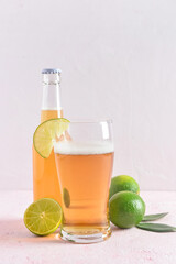 Glass and bottle of cold beer with lime on light background