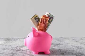 Piggy bank with euro banknotes on grunge grey table near wall