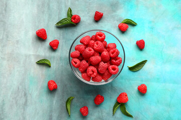 Glass bowl with fresh raspberries and mint on blue background