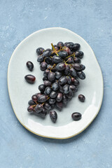 Plate with sweet black grapes on blue background
