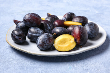 Plate with fresh plums on blue background