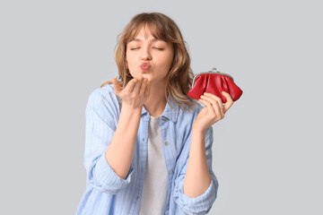 Beautiful young woman with red purse blowing kiss on grey background