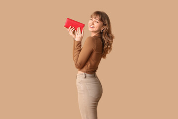Beautiful young woman holding red wallet on brown background