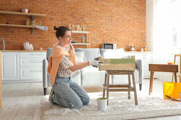 Young woman with brush painting wooden box at home