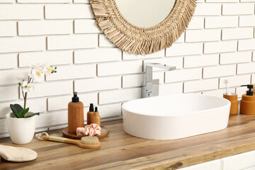 Sink and bath supplies on chest of drawers near white brick wall in bathroom