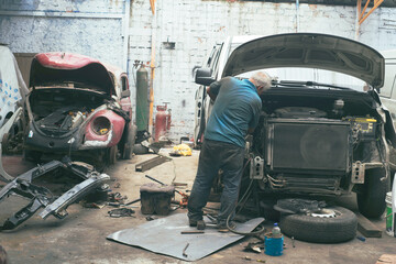 A senior men car mechanic inspects and repairs a car body to troubleshoot problems in a workshop.