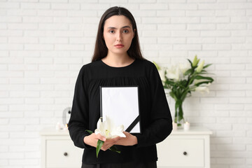 Young woman with funeral lily flower and photo frame in room