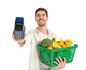 Young man with full shopping basket and payment terminal on white background