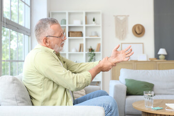 Senior man suffering from Parkinson syndrome on sofa at home