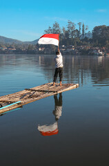 Rear View Of Young Male Standing On Bamboo Raft Proudly Waving Indonesian Flag