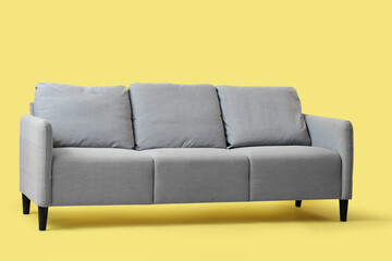 Comfortable grey sofa on yellow background