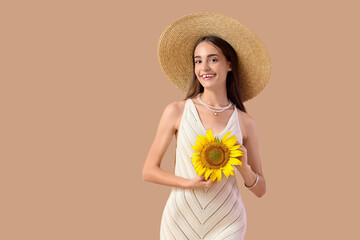 Pretty young woman with sunflower on beige background