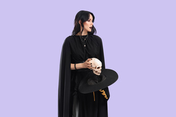 Beautiful young woman dressed as witch for Halloween with human skull on purple background