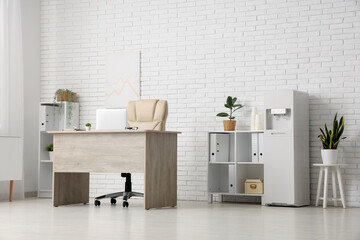 Interior of light office with modern water cooler, workspace and shelving unit