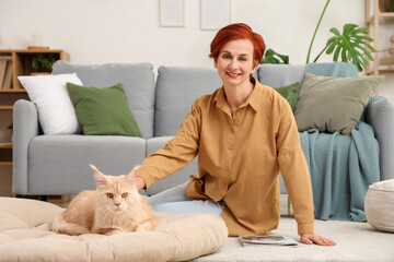 Mature redhead woman with cute Maine Coon cat sitting on floor at home