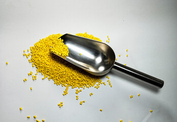 Yellow plastic masterbatch, polymer carries colorful pigments with small scoops poured into a white...