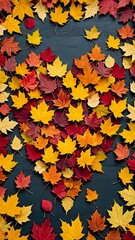 Scattered red, orange, and yellow autumn leaves loosely forming heart shape on dark textured wooden background. Seasonal concept
