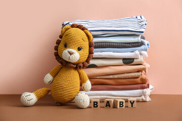 Stack of baby clothes with toy on table against beige background