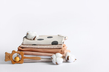 Stack of baby clothes with rattle and cotton flowers on white background