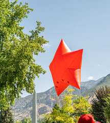 A large red star-shaped inflatable balloon floats above a crowd during a patriotic outdoor parade