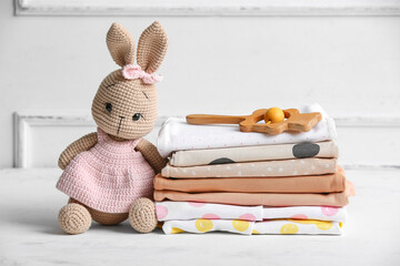 Stack of baby clothes with rattle and toy on table near light wall