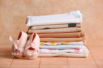 Stack of baby clothes with booties on table near grunge wall