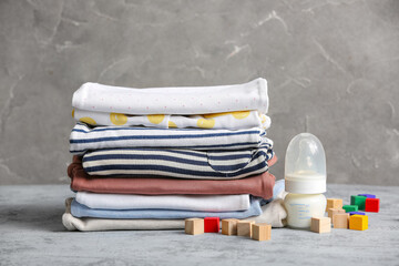 Stack of baby clothes with milk and cubes on table against grunge background