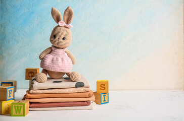Stack of baby clothes with toy bunny and cubes on table against grunge background