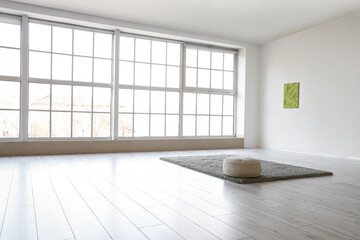 Pouf with carpet and painting on light wall in big room