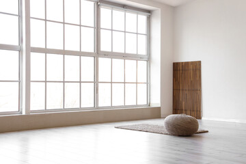 Pouf on carpet and folding screen near light wall in big room