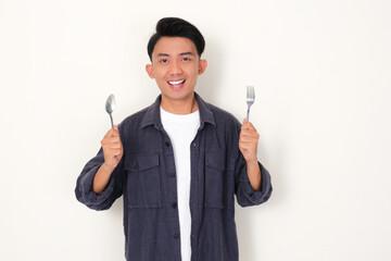 Young Asian man smiling at the camera while holding spoon and fork