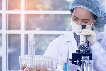 Woman scientist wearing white glue and a hair cap working with laptop, experiment at laboratory.